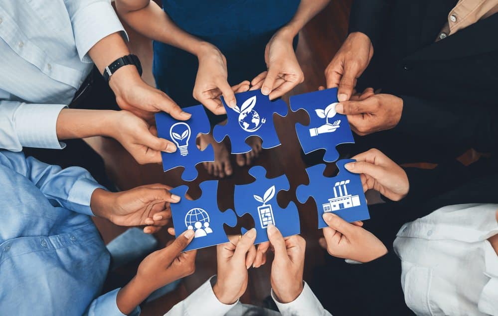 Mãos de diferentes pessoas unidas formando um quebra-cabeça com peças que simbolizam sustentabilidade, meio ambiente, energia renovável e responsabilidade social.