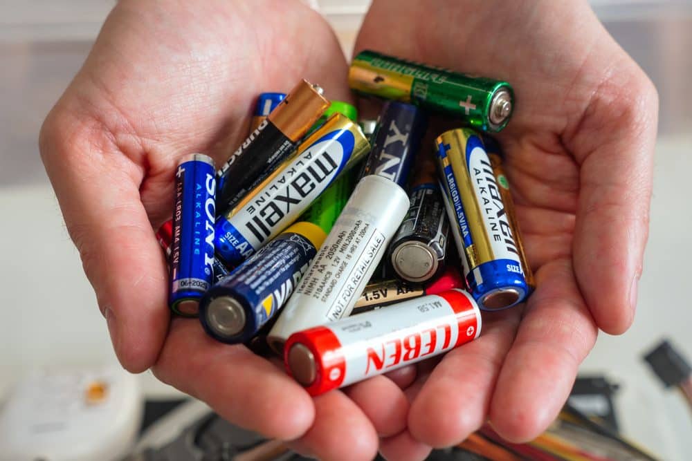 reaproveitamento materiais eletronicos Conjunto de pilhas e baterias acumuladas nas mãos, representando ações de reaproveitamento de materiais.