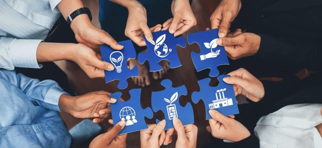 Mãos de diferentes pessoas unidas formando um quebra-cabeça com peças que simbolizam sustentabilidade, meio ambiente, energia renovável e responsabilidade social.